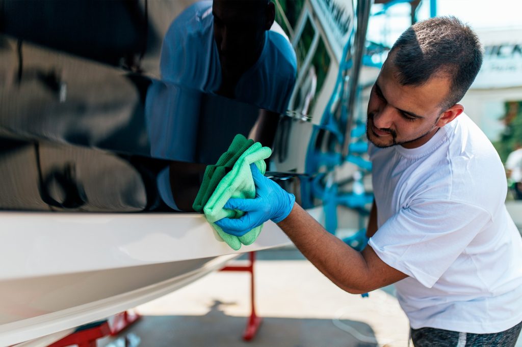 Man in white t-shirt cleaning his boat's hull with a green microfiber cloth in preparation for a boat show