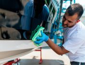 Hombre con camiseta blanca limpiando el casco de su barco con un paño de microfibra verde para prepararlo para un salón náutico.