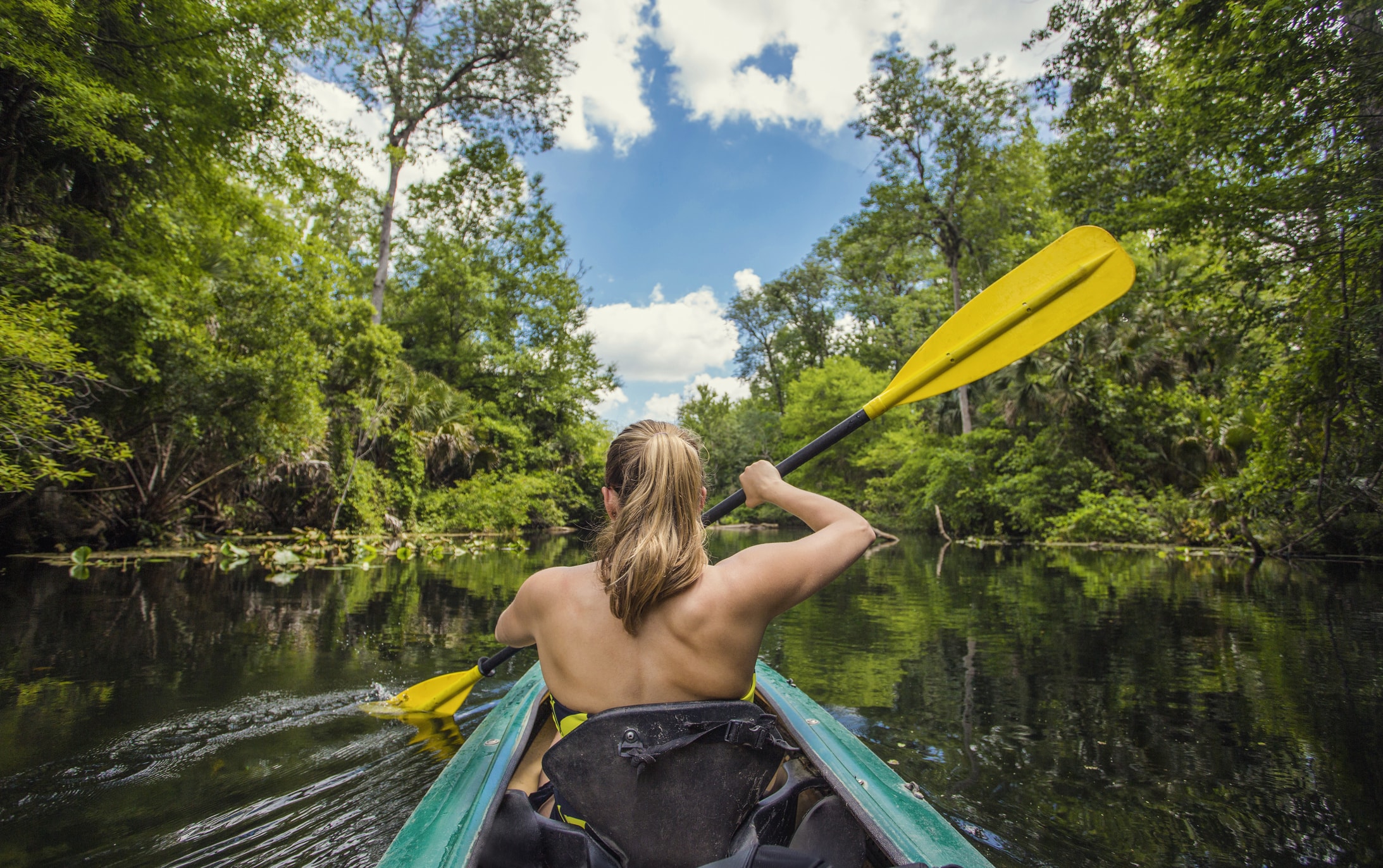 Mujer en kayak verde remando por un tranquilo río rodeado de árboles en Florida