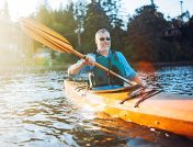 Hombre en un kayak naranja sonriendo y remando por el agua en los Finger Lakes