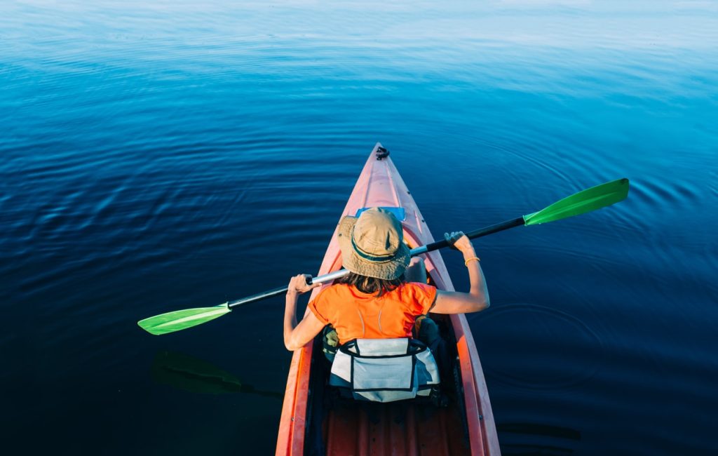 Woman in orange shirt kayaking facing away from camera