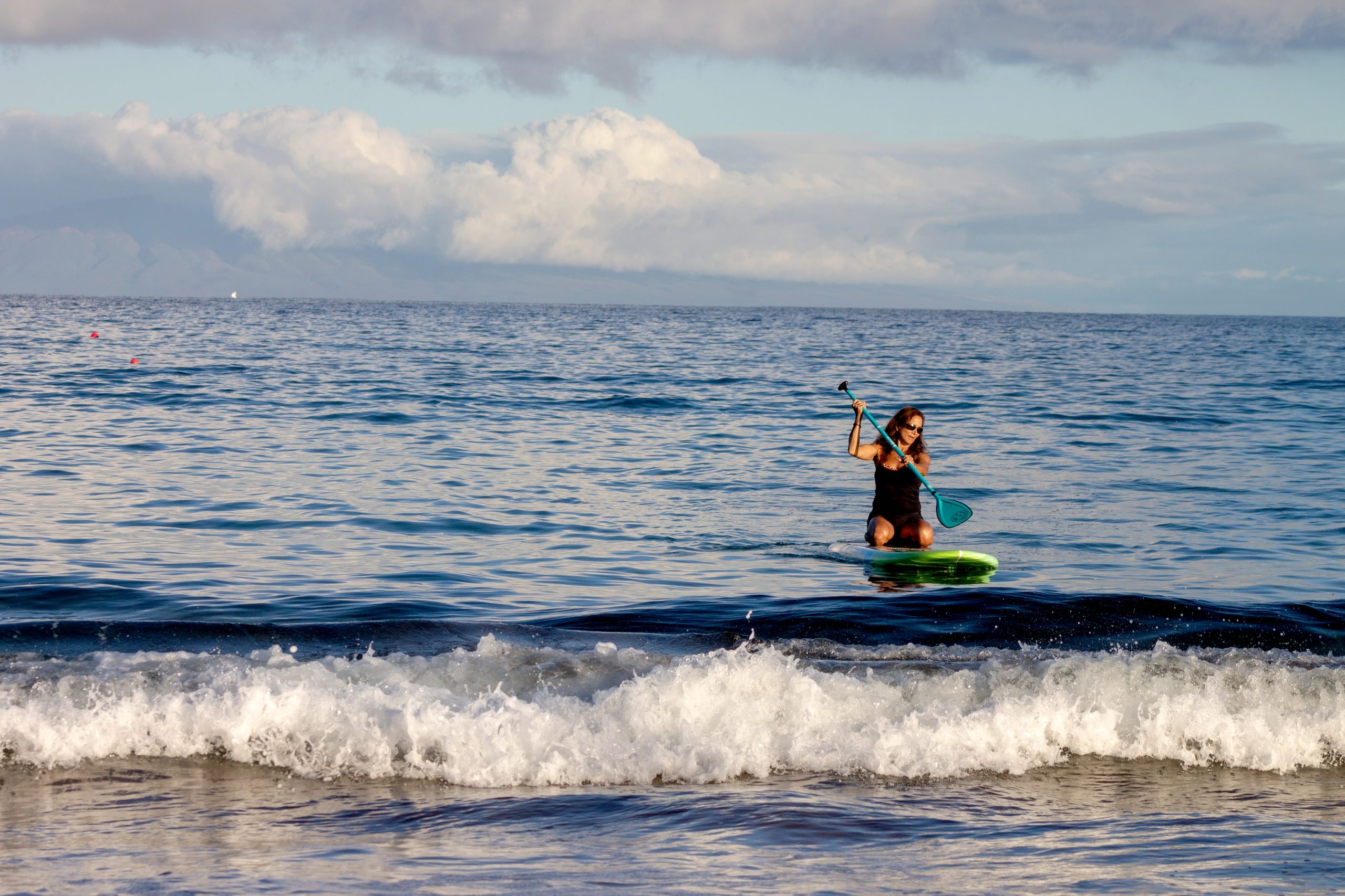 Kvinne kneler på paddleboard på stranden
