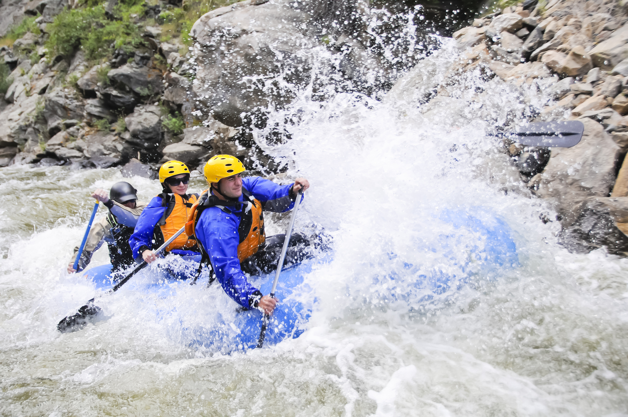 Un grupo de kayakistas con chaquetas, cascos y chalecos salvavidas remando en un gran kayak azul por rápidos de aguas bravas.