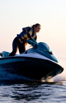 Woman in yellow life vest driving a green and white jet ski at high speeds