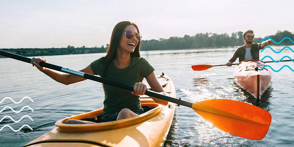 A young couple of kayakers smiling and laughing while paddling through calm water on a sunny day in Michigan