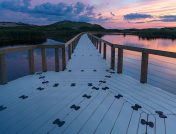 Wooden bridge walkway going over a scenic body of water with a colorful sky backdrop