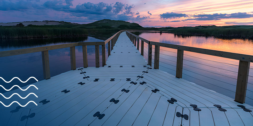 Wooden bridge walkway going over a scenic body of water with a colorful sky backdrop
