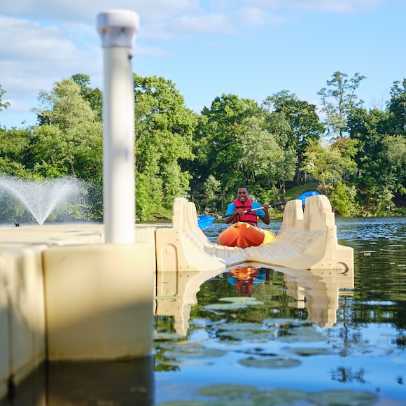 man, smiling, paddling his kayak onto an EZ Dock floating dock designed for kayaks